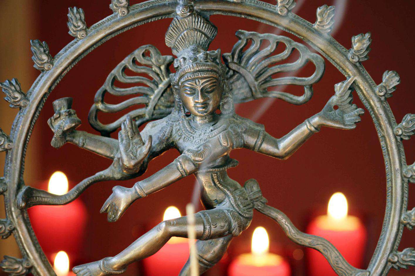 A statue of shiva with candles in the background.